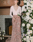 Woman in a white top and floral skirt standing in front of a decorated floral wall.