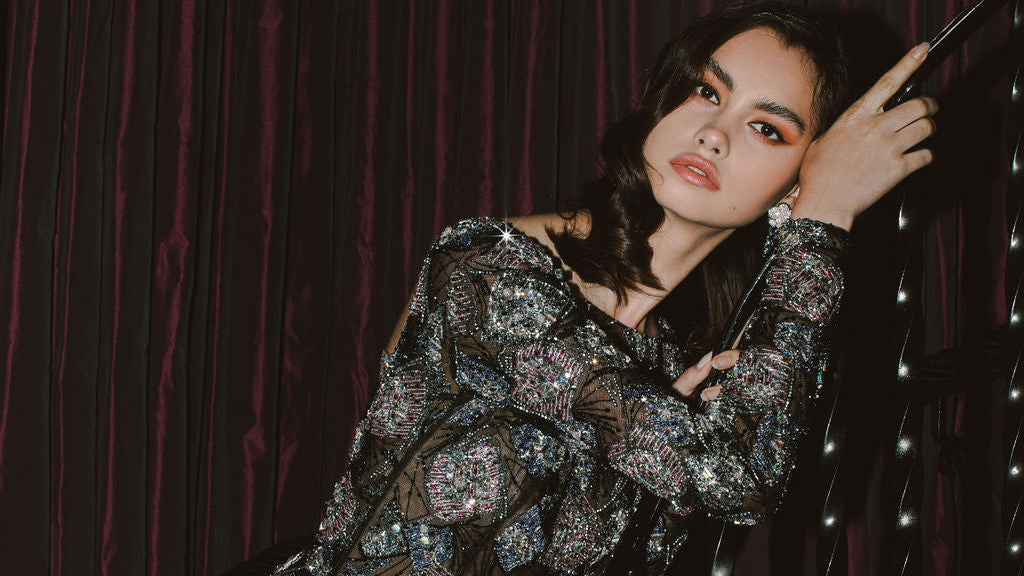 Woman in a sparkling dress against a dark curtain with string lights