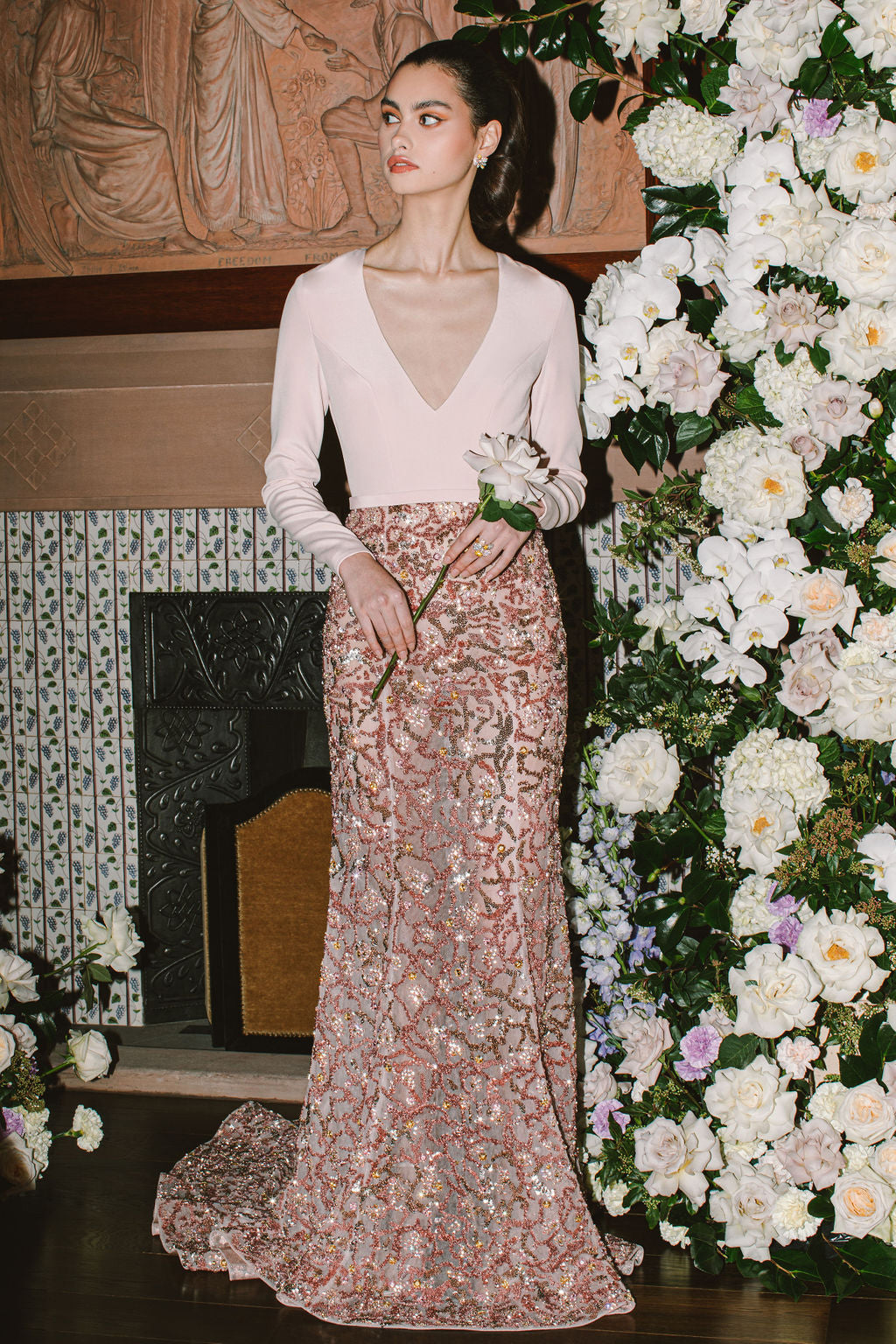 Woman in a white top and floral skirt standing in front of a decorated floral wall.
